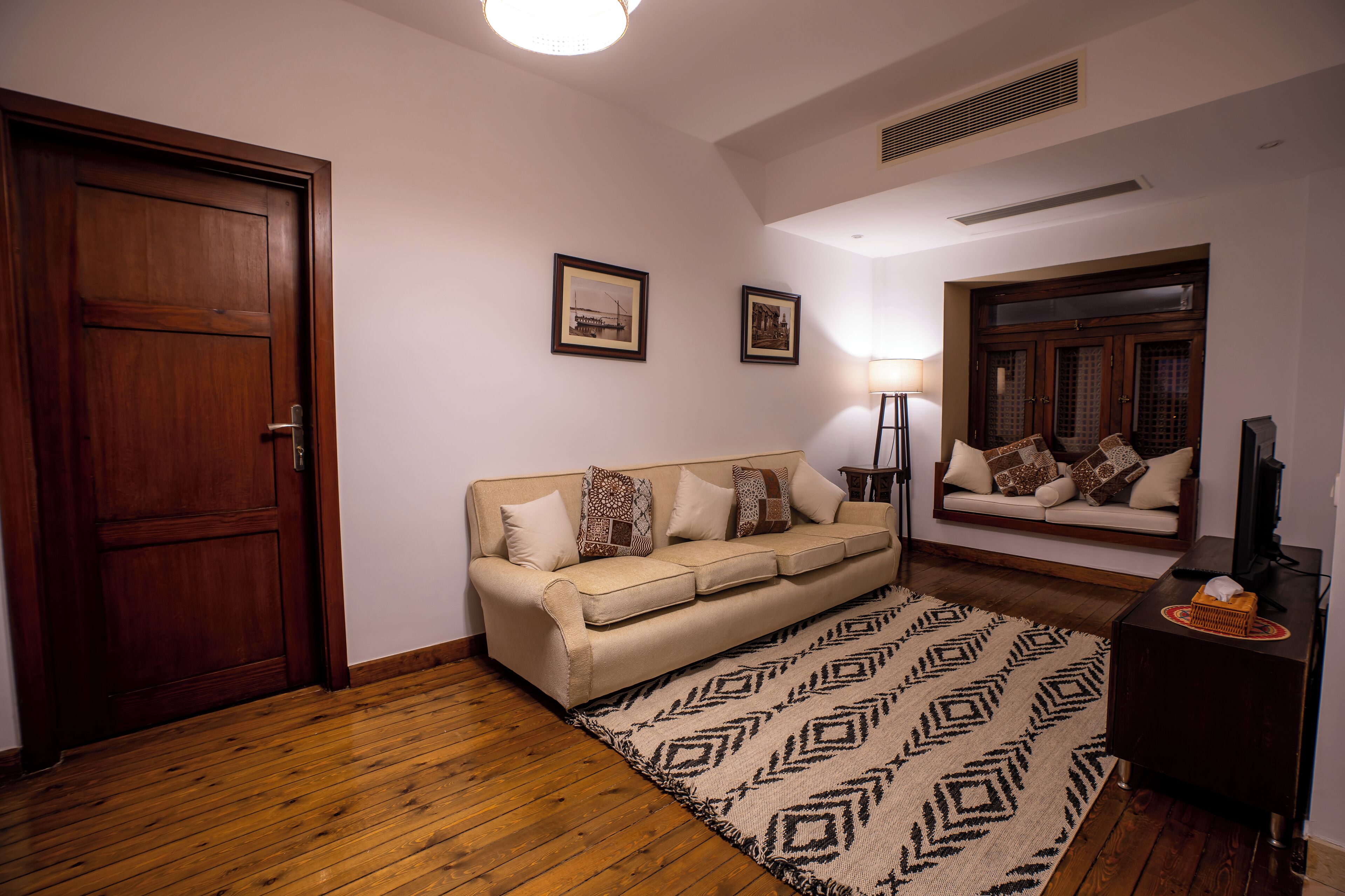 A living room with a wooden floor, a beige sofa, patterned rug, and a television on a wooden stand.