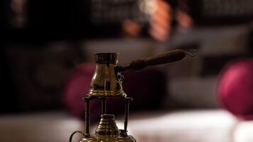A brass teapot and three glasses on a tray, with a blurred background of a room with a window and a couch.