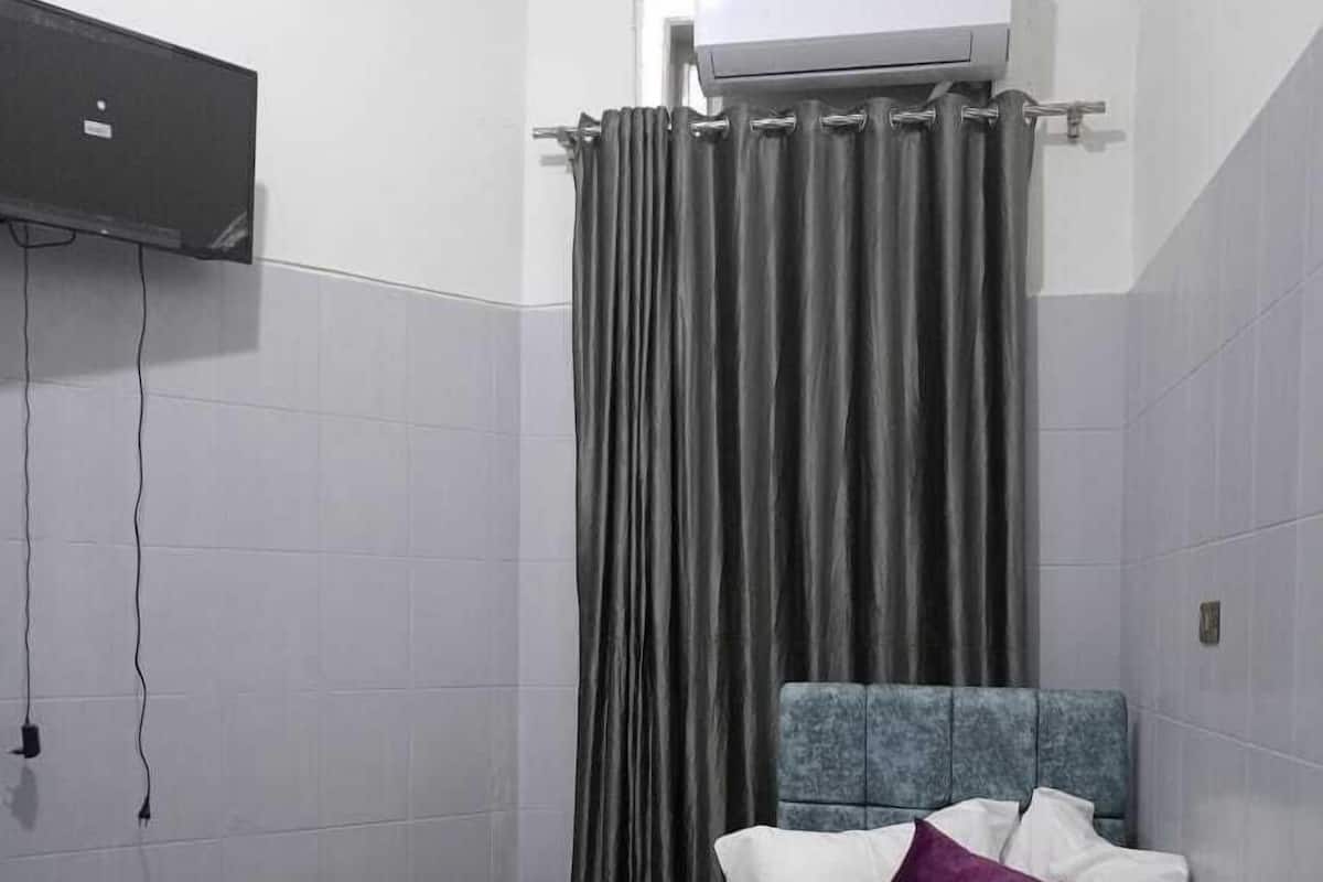 A small, compact room with two single beds, a grey curtain, and an air conditioning unit mounted on the wall.