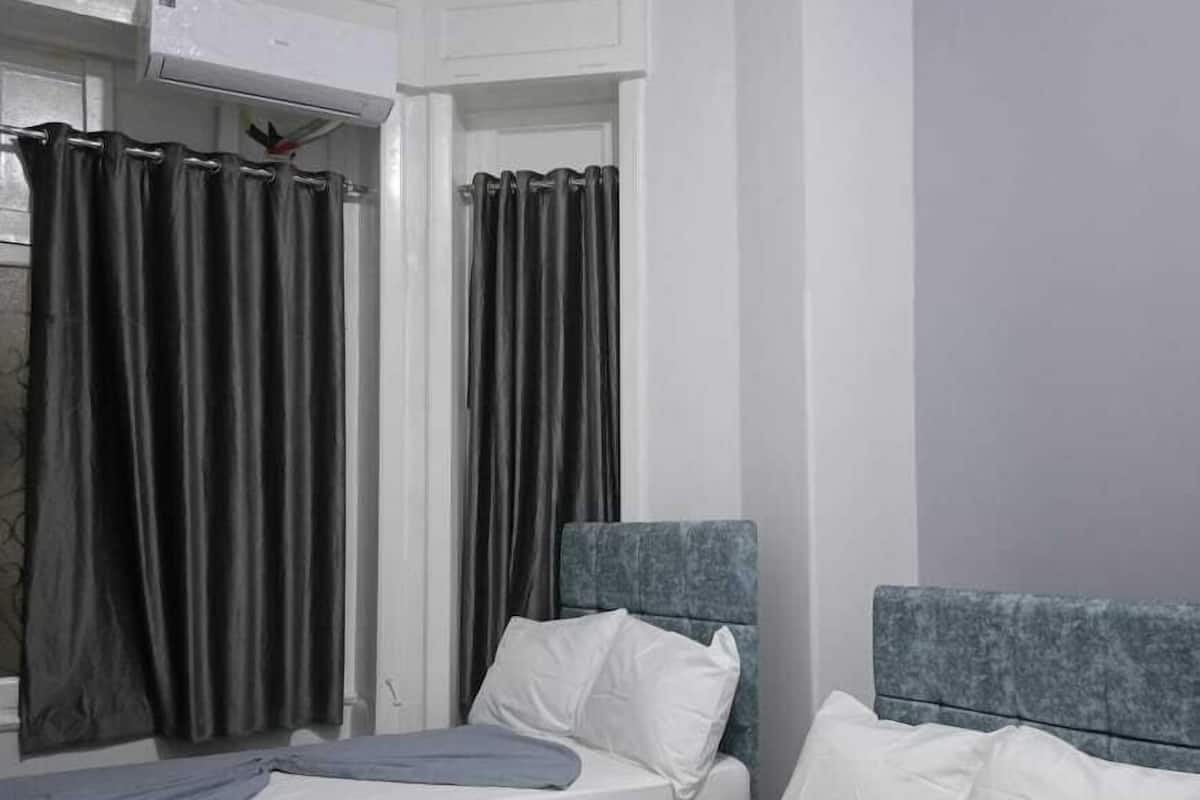 A hotel room with two single beds, grey headboards, white bedding, and grey curtains.