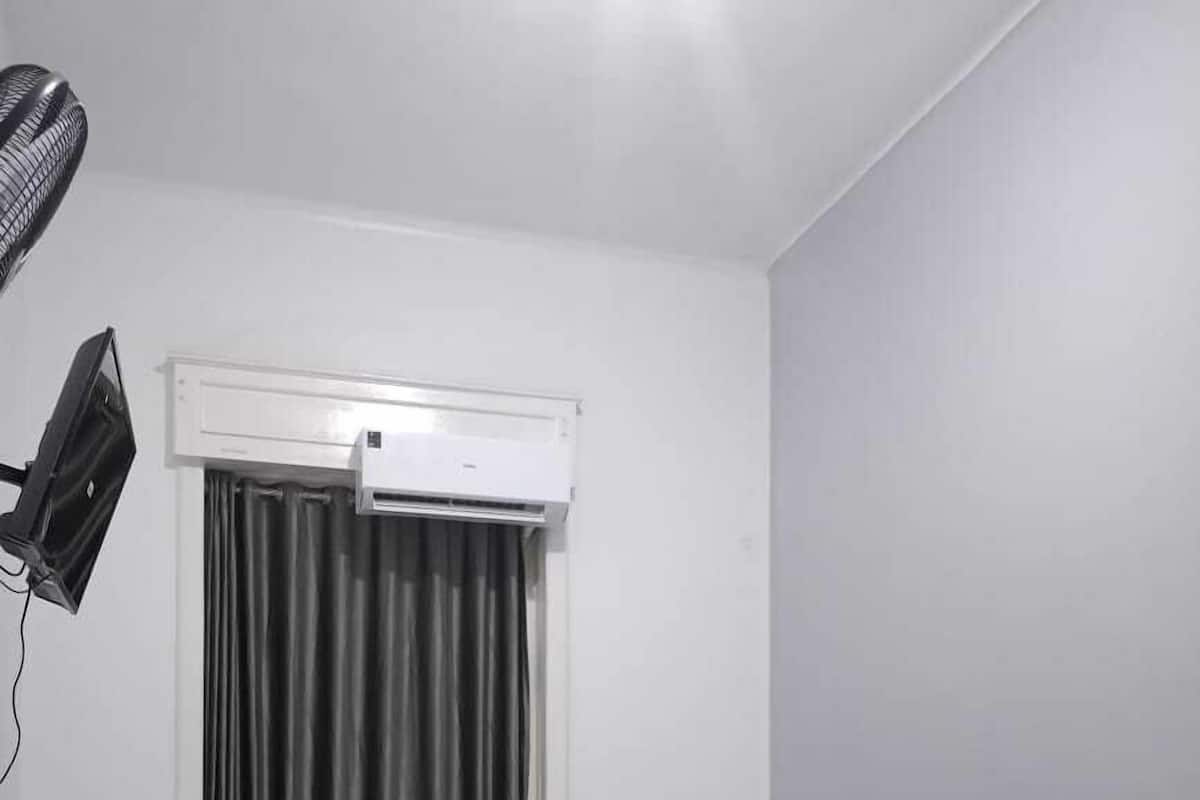 A room with two single beds, a ceiling fan, an air conditioning unit, and a TV mounted on the wall.