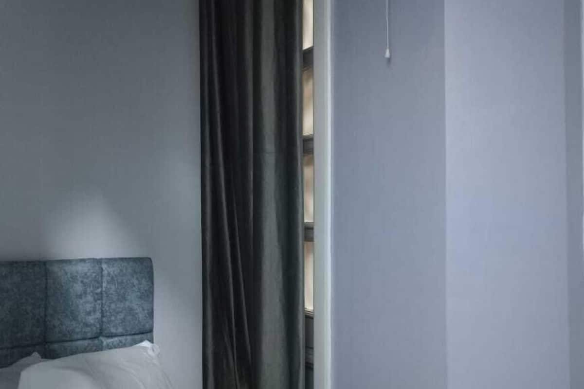 A hotel room with a bed, a headboard, a nightstand, and a window with curtains.