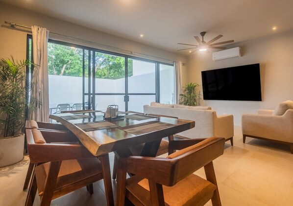 Una sala de estar moderna con una mesa de comedor de madera, sofás color beige y un televisor de pantalla plana montado en la pared.