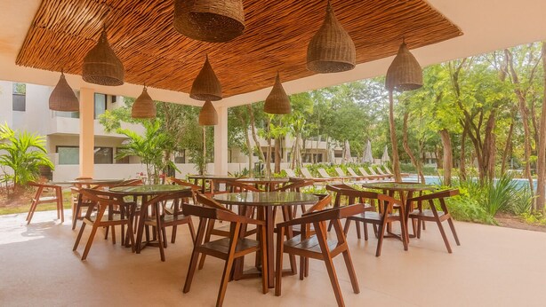 Un espace de restauration en plein air, avec des tables et des chaises rondes, entouré d’une végétation luxuriante et d’une piscine.