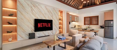 Una sala moderna con un televisor de pantalla plana grande montado en una pared de mármol, un sofá, una mesa de centro y una cocina al fondo.