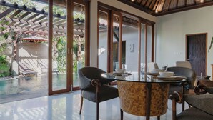 Un espace repas avec une table en verre, des chaises et une vue sur une piscine et un espace extérieur.