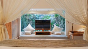 Une chambre avec un grand lit, une télévision et une vue sur une végétation tropicale.