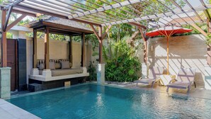 Un espace piscine doté d’un coin salon couvert et de chaises longues.