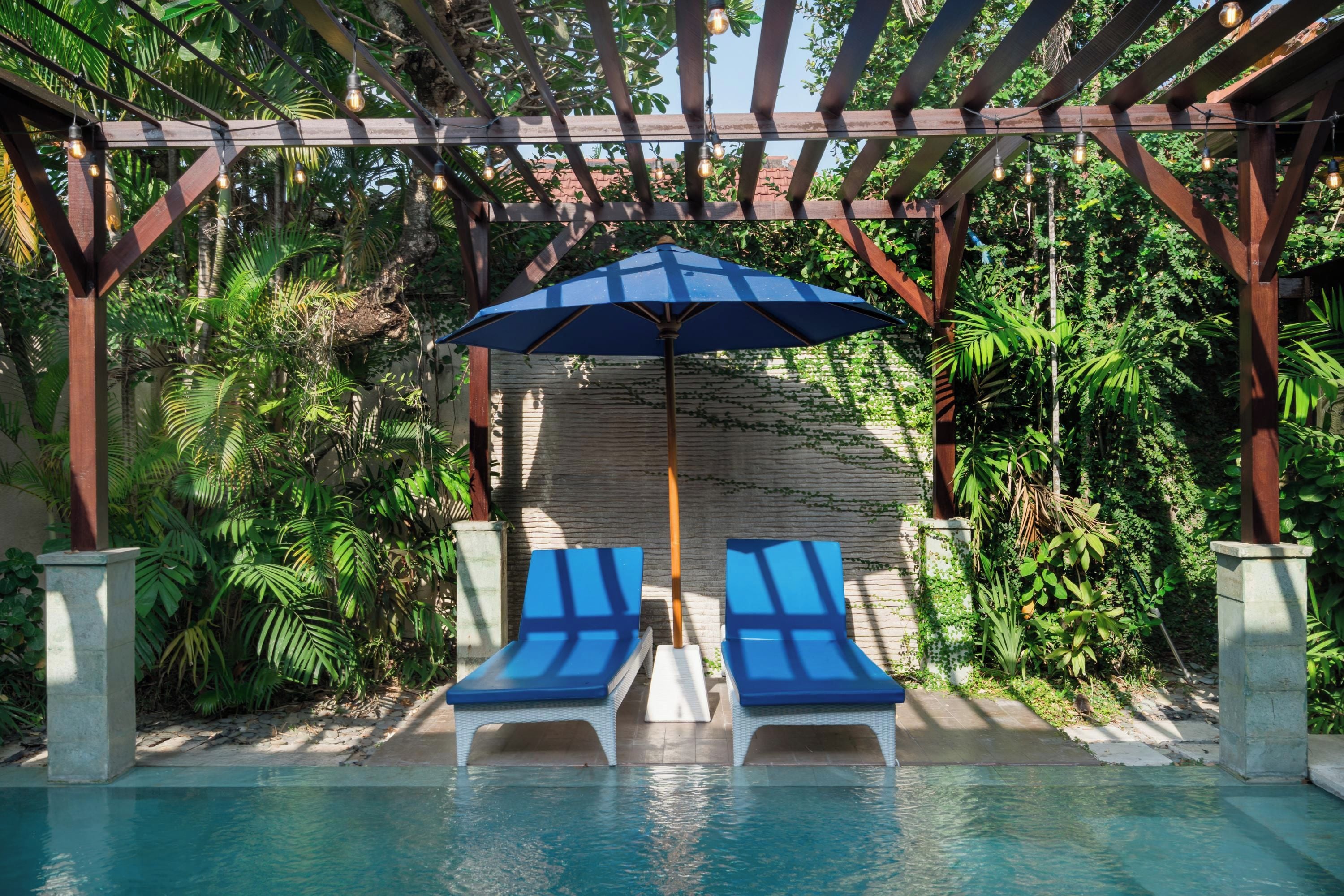 Área da piscina com duas espreguiçadeiras e um guarda-sol azul.