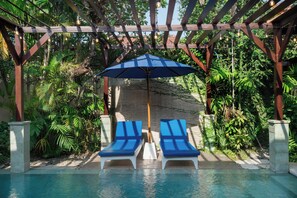 A pool area with two lounge chairs and a blue umbrella.