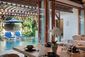 A poolside area with lounge chairs, a dining table set for two, and a view of the pool. - Jepun Villa by Betterplace (Seminyak)