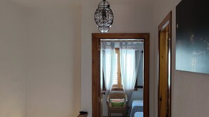 A hallway with a wooden door frame, a hanging light fixture, and a bed with patterned bedding in the background.
