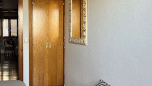 A room with a bed, a wooden wardrobe, a bench with a striped pillow, and a mirror on the wall.