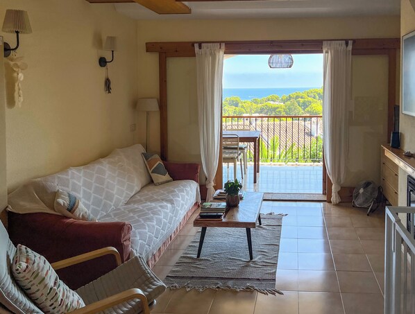 A cozy living room with a sofa, a coffee table, and a view of a balcony with a railing and a table.