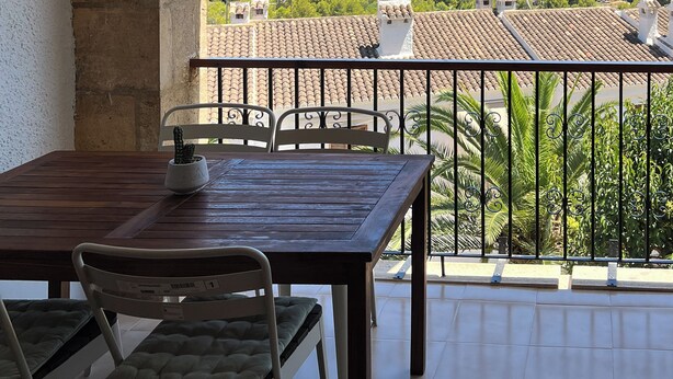 A balcony with a view of the sea, a table with chairs, and a hanging light fixture.