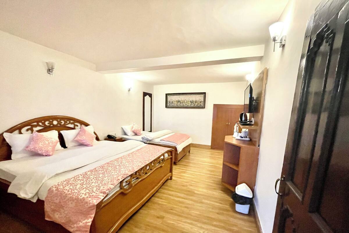 A bedroom with two wooden beds, a wooden wardrobe, a small desk with a chair, and a trash bin.