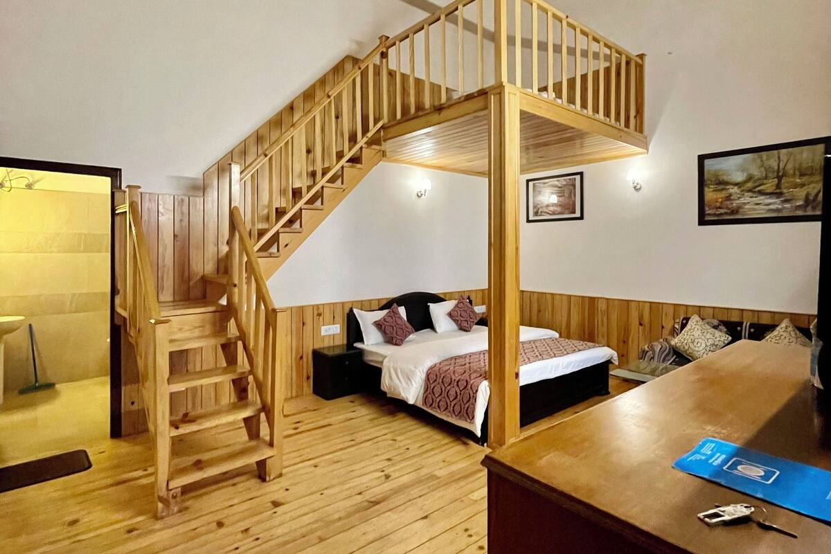 A wooden staircase leading to a loft bedroom with a bed, a desk, and a view of the outdoors.