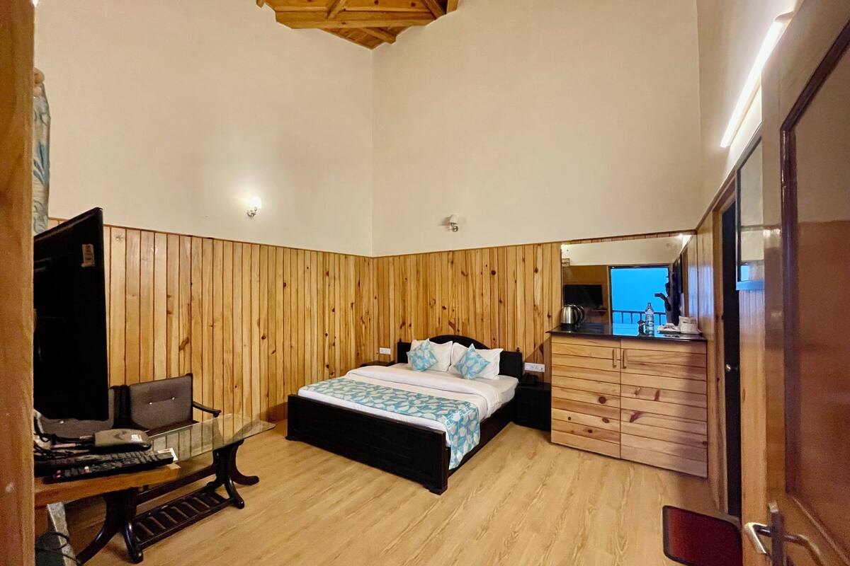 A bedroom with a wooden paneled wall, a bed with a blue and white patterned bedspread, a desk with a computer, and a mirror.