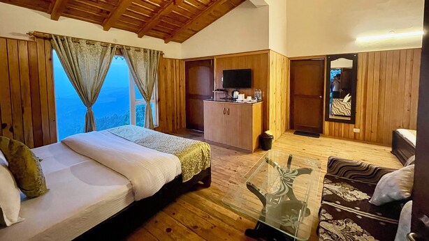 A room with a bed, a sofa, a glass table, a TV, and a view of the outdoors. - Shri Shail Inn (Dhari)