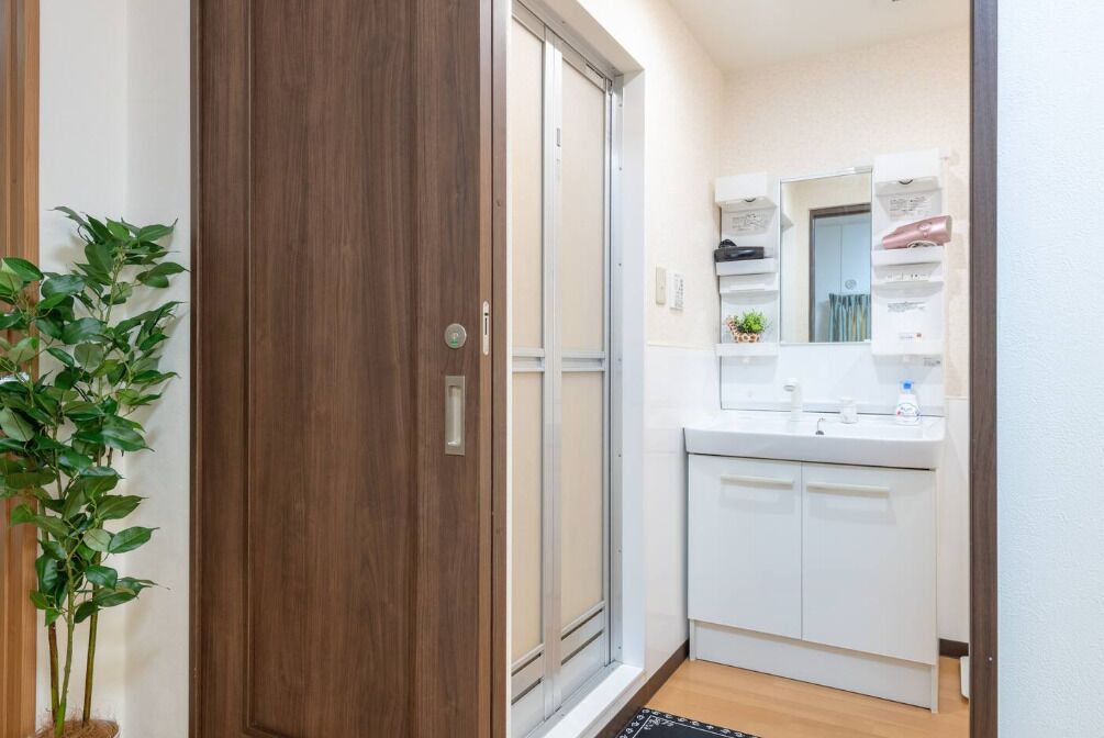 Un pasillo con una puerta de madera, una puerta corredera de vidrio y un baño blanco con lavabo y espejo.