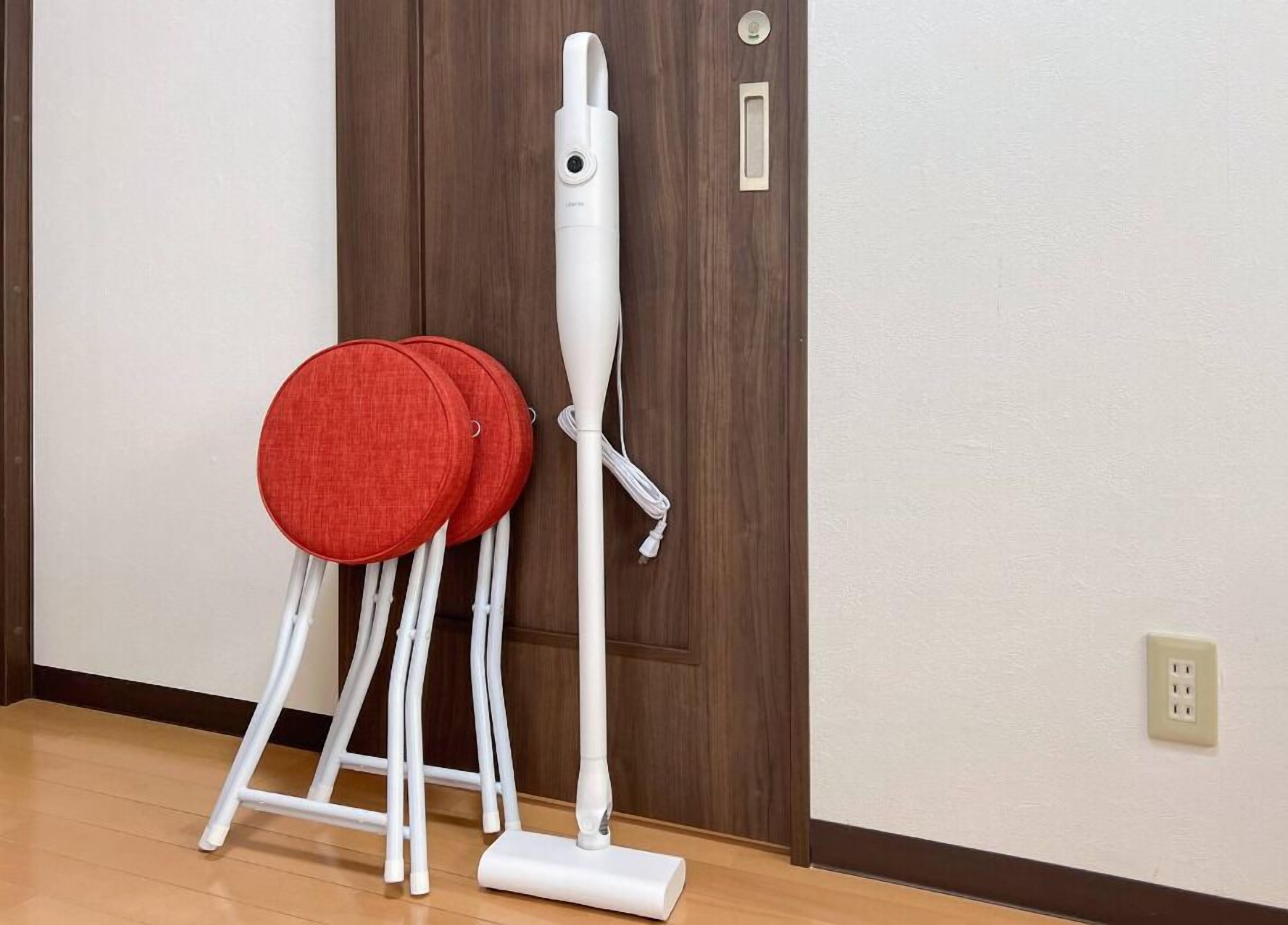 Calentador blanco de pie con asiento de tela roja, ubicado frente a una puerta de madera.