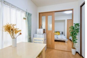 A compact room with a bed, a microwave, a small table with a vase of dried flowers, and a potted plant. - 6 Minutes to Shinjuku Station by Train, Max 4 People (Tokyo)