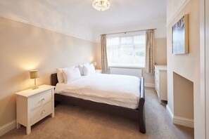 Een slaapkamer met een bed, nachtkastje, lamp, raam met gordijnen en een radiator.