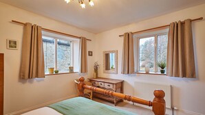 Un dormitorio con una cama de madera, un aparador y dos ventanas con cortinas.