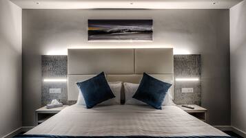 A modern hotel room with a large bed, two nightstands, a headboard with integrated lighting, and a painting above the bed.