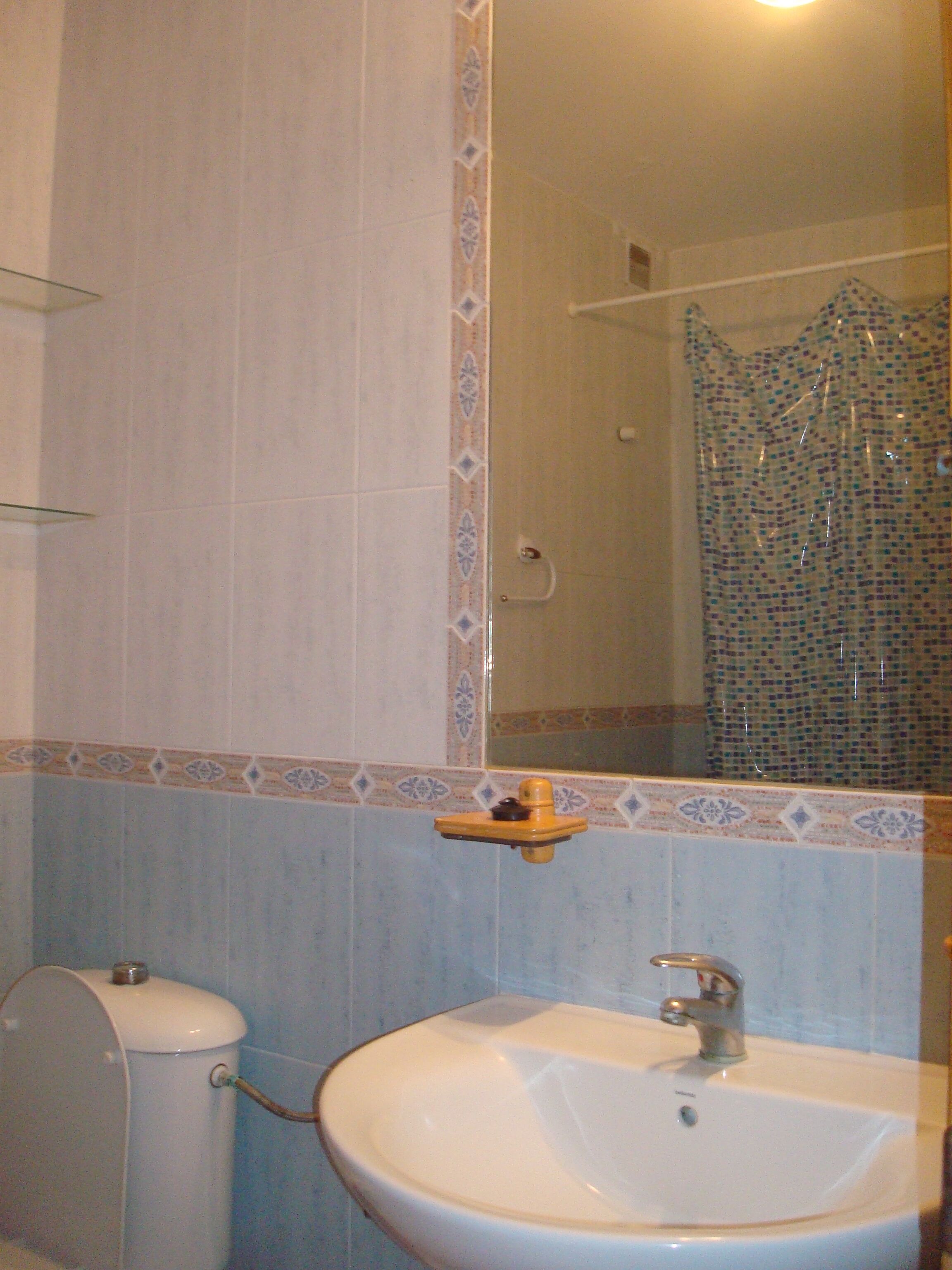 A bathroom with a white sink, a toilet, and a shower with a mosaic tile wall.