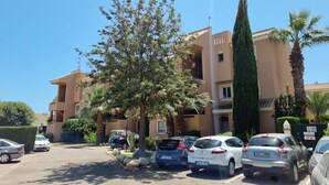 A parking lot with several cars, a building with a beige facade, and a tall green tree. - Ground floor naturist studio with terrace (Playas de Vera)
