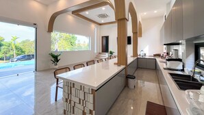 A modern kitchen with a central island, built-in appliances, and a view of the outdoors. - Celine House by Craft Village (Koh Samui)