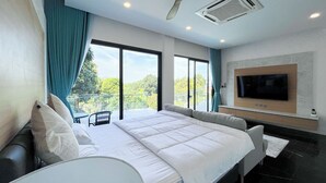 A modern hotel room with a large bed, a ceiling fan, an air conditioning unit, a flat-screen TV mounted on the wall, and a balcony with a view of trees. - Celine House by Craft Village (Koh Samui)