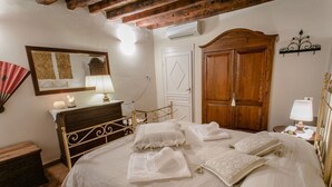 A bedroom with a bed, wooden wardrobe, bedside table, lamp, and a mirror on the wall. - FLORENCE TOWER APARTMENT (Firenze)