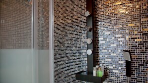 A bathroom with a tiled wall, a shower area, and a shelf with toiletries. - FLORENCE TOWER APARTMENT (Firenze)