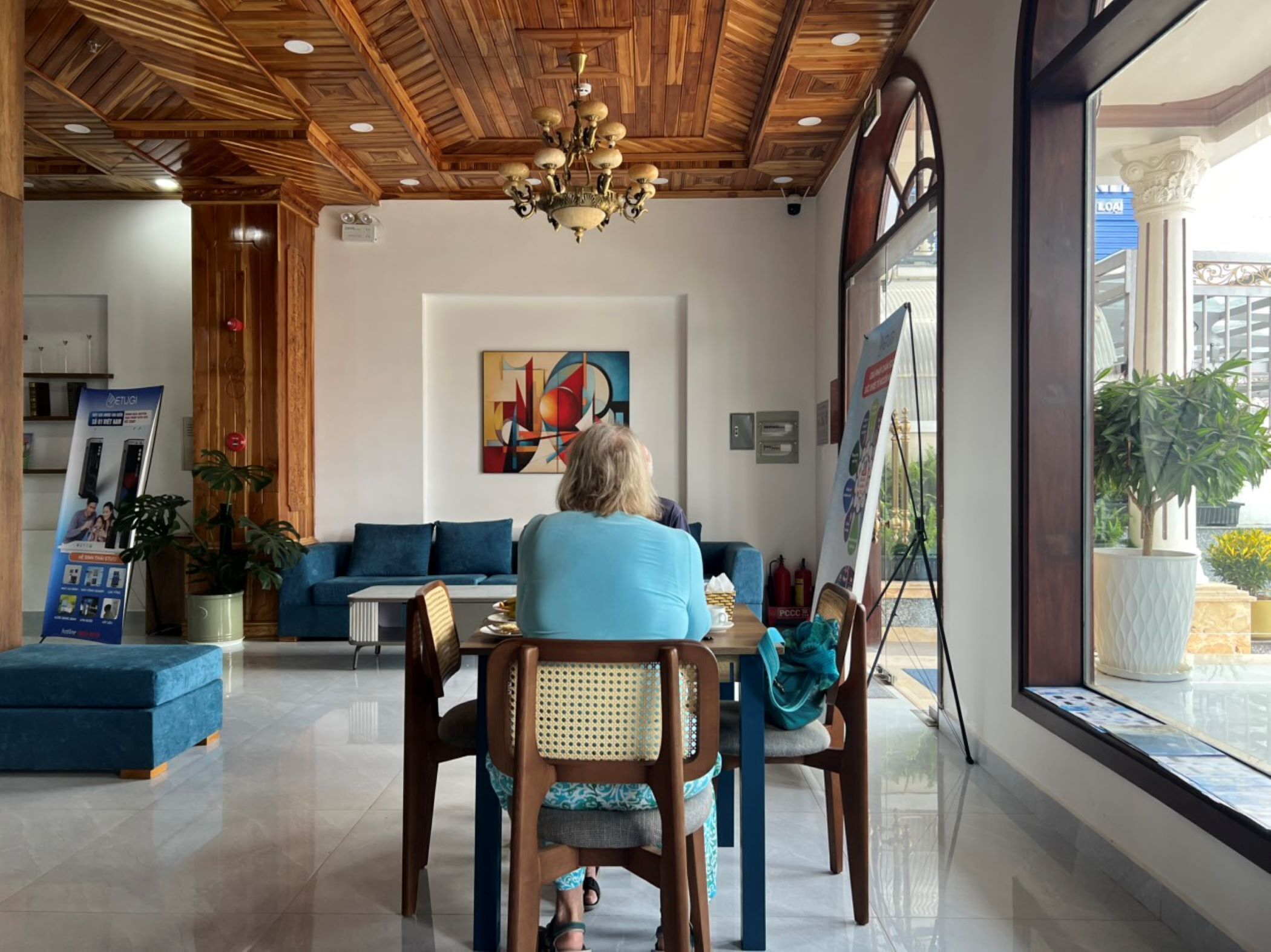 A modern interior with a wooden ceiling, a blue sofa, a dining table with chairs, and a large window with a view.