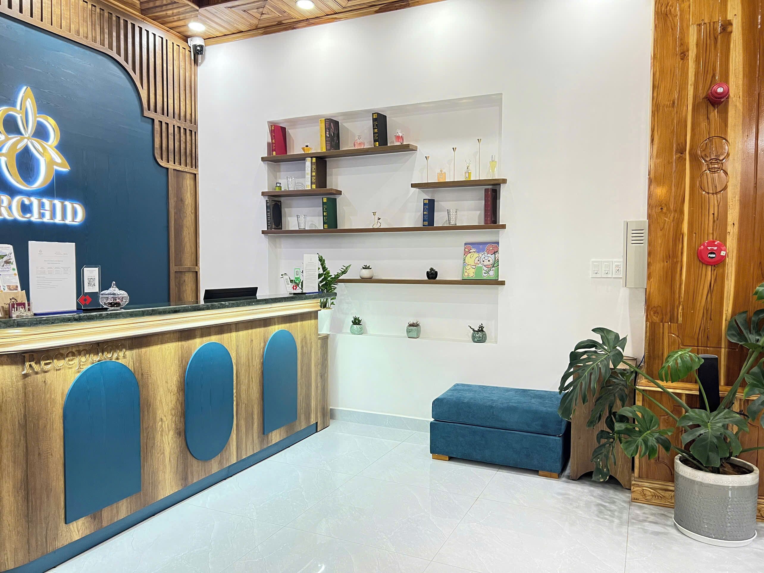 Un área de recepción con un mostrador de madera, asientos acolchados azules y estantes con libros y objetos decorativos.