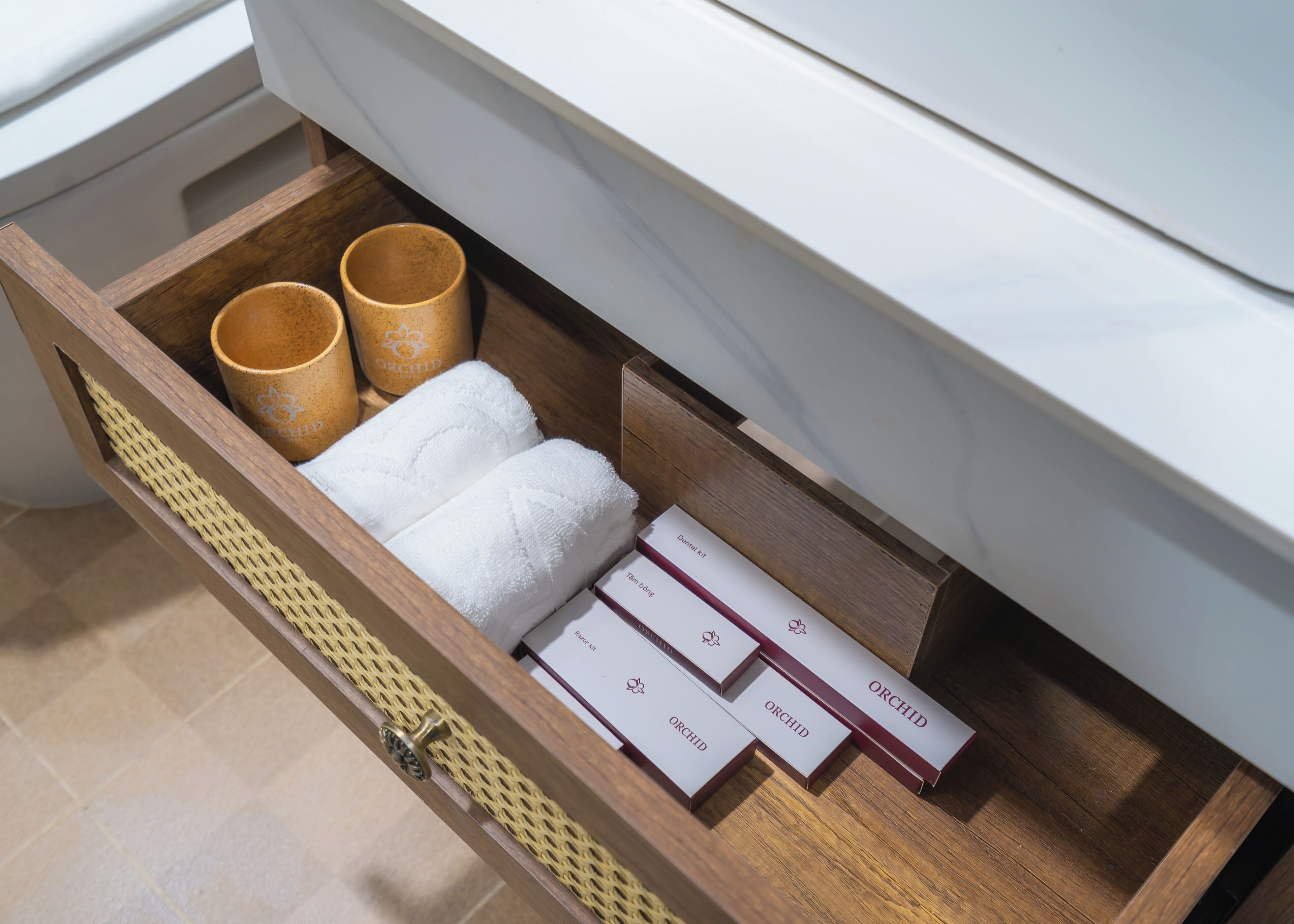 A wooden drawer with a woven basket, two brown ceramic cups, a white towel, and several white boxes with the word "ORCHID" on them.