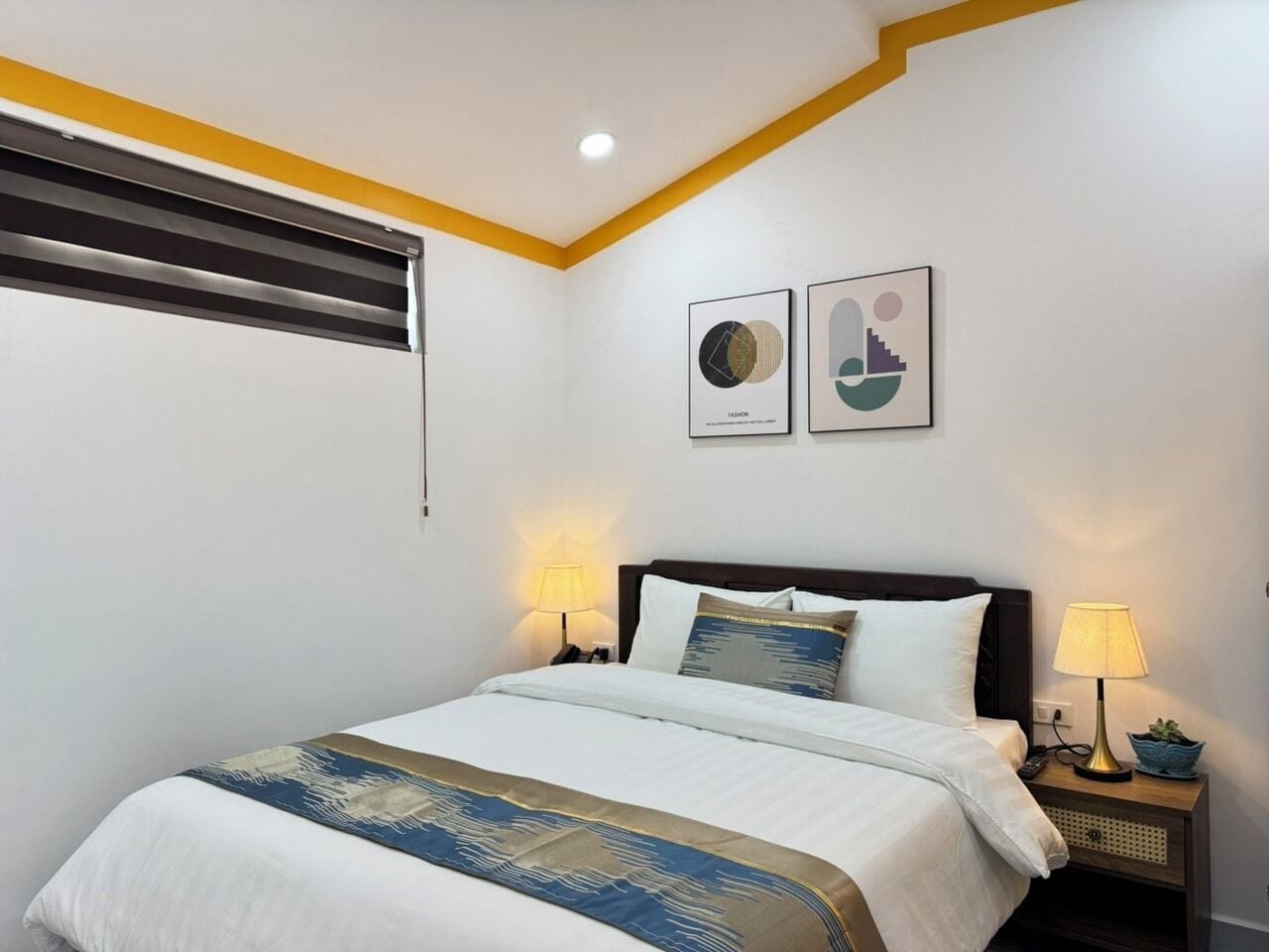 Ein Hotelzimmer mit einem Bett, zwei Nachttischlampen, einer Wandklimaanlage und zwei gerahmten Bildern an der Wand.