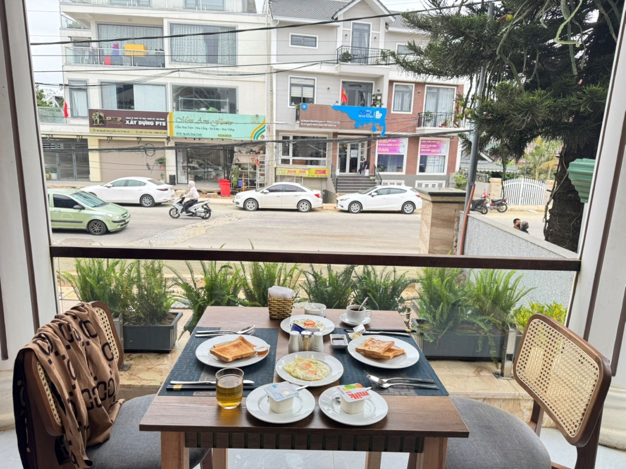A dining area with a table set for two, overlooking a street with cars and a building with various signs.