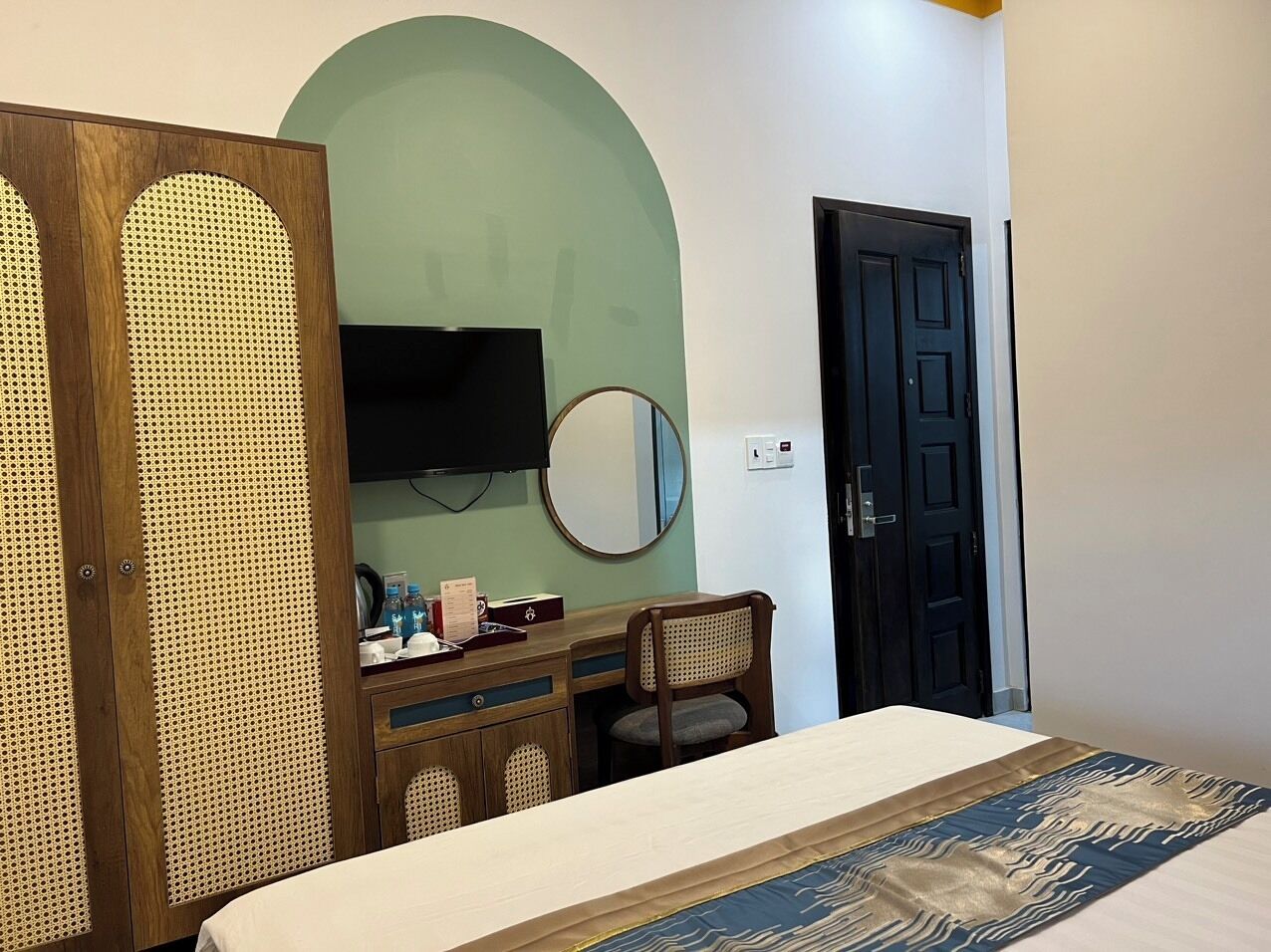 A bedroom with a bed, a desk with a chair, a television, and a door.