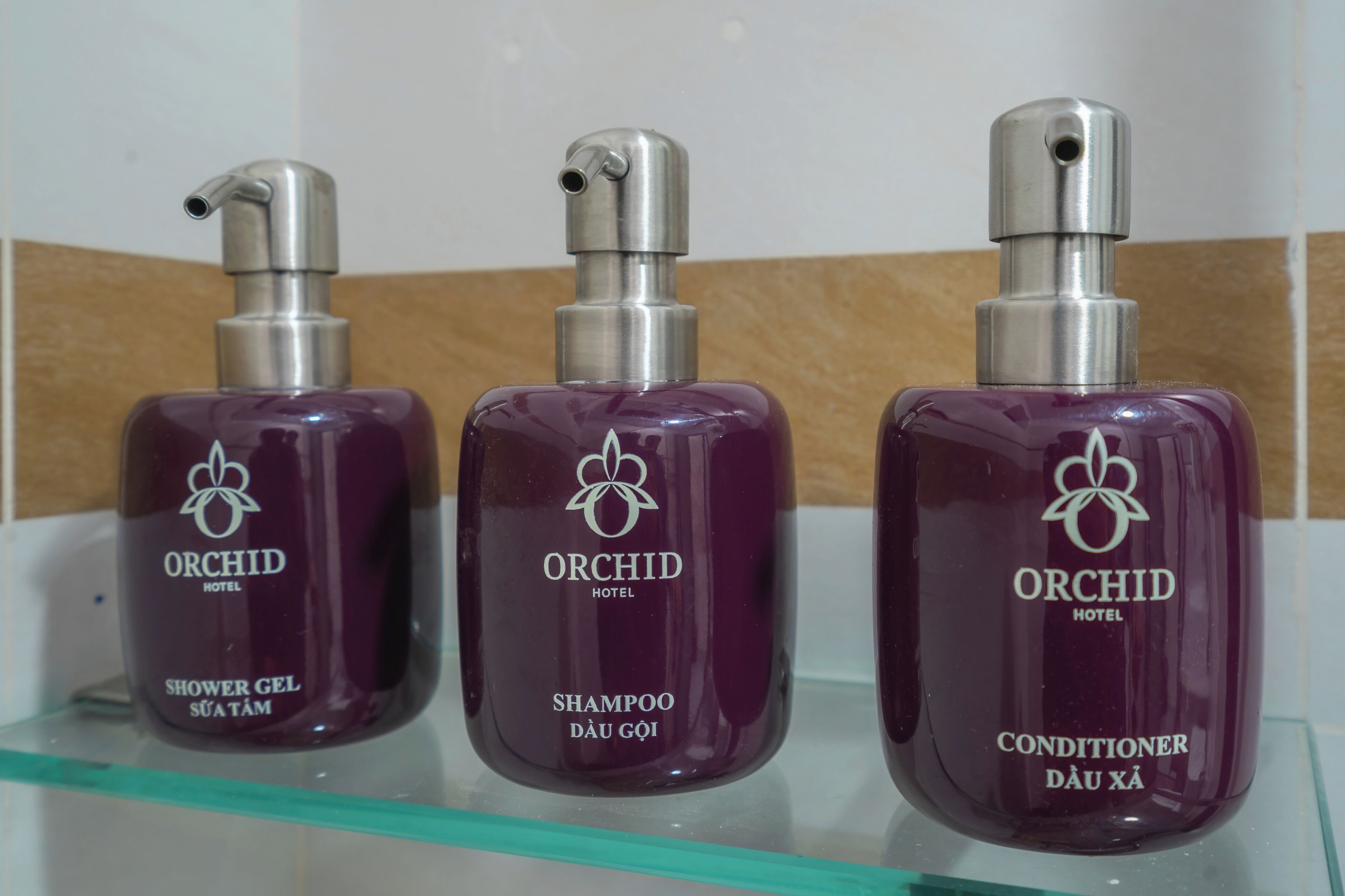 Tres botellas de productos del Hotel Orchid: gel de ducha, champú y acondicionador.