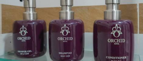 Tres botellas de productos del Hotel Orchid: gel de ducha, champú y acondicionador.