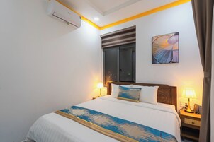 Habitación de hotel con cama, lámparas de noche, ventana con persianas, aire acondicionado y una obra de arte colgada en la pared.