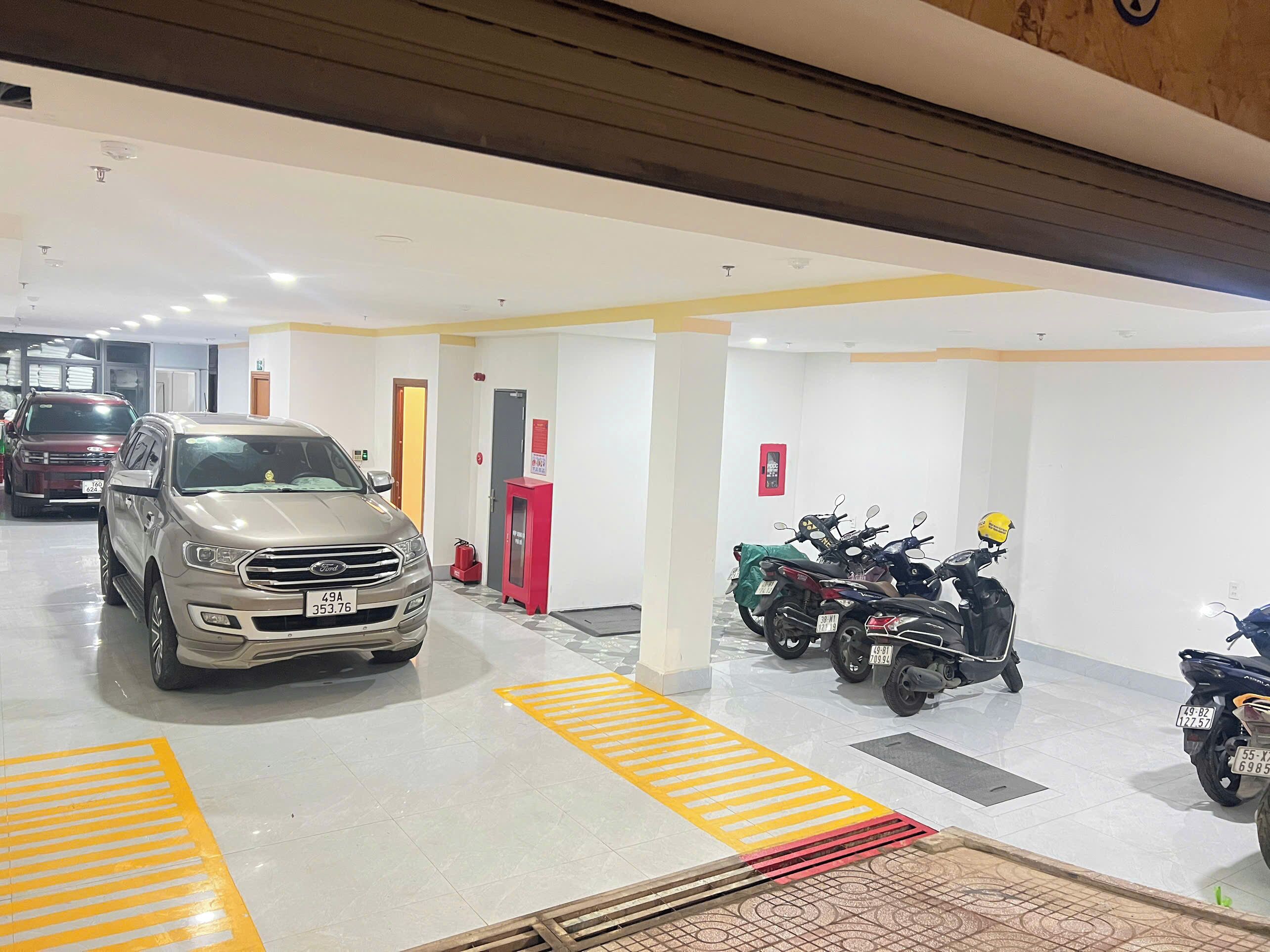 A parking garage with multiple vehicles, including cars and motorcycles, and a fire extinguisher near the entrance.