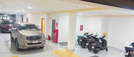 A parking garage with multiple vehicles, including cars and motorcycles, and a fire extinguisher near the entrance.