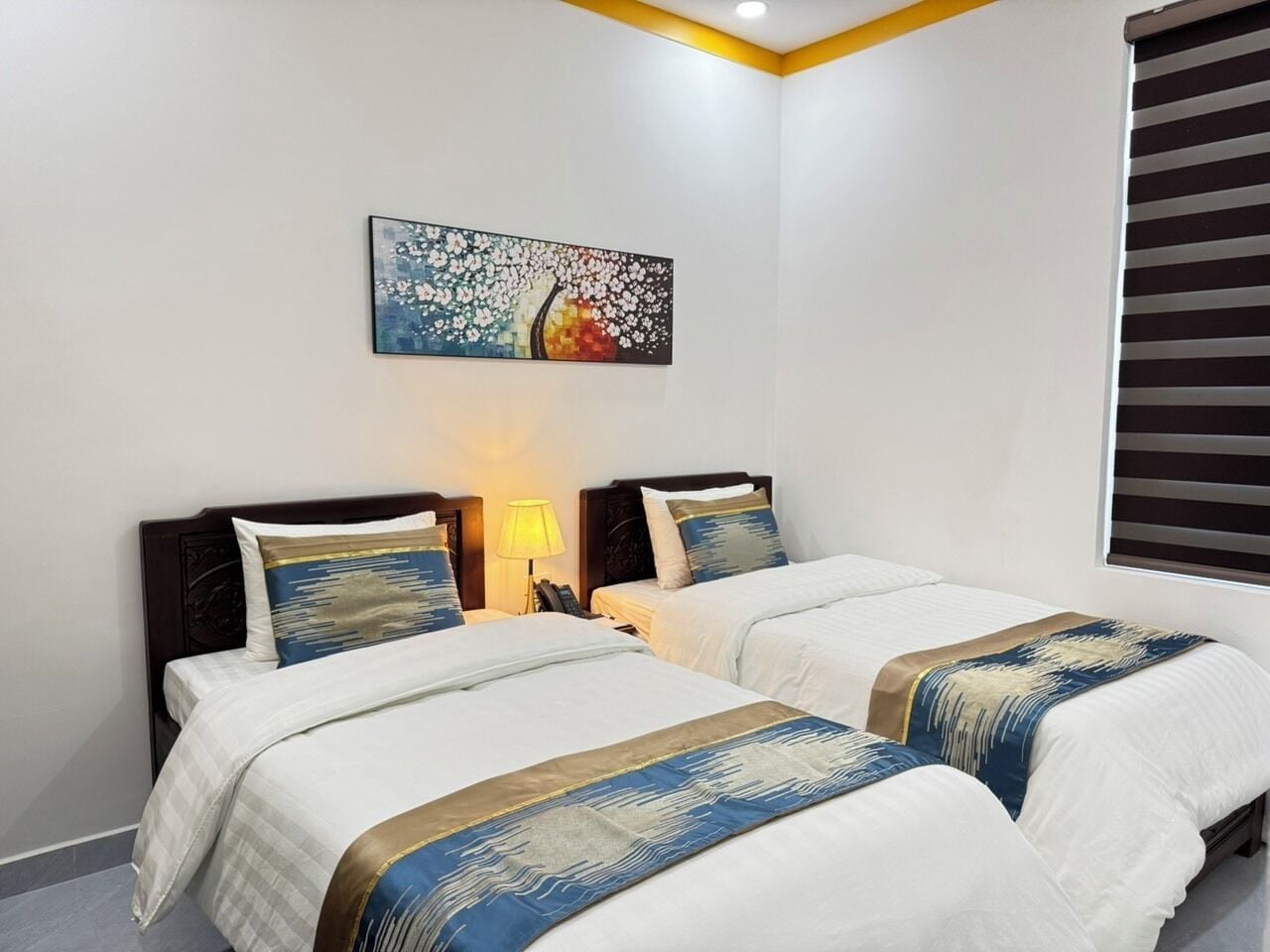 A hotel room with two beds, a nightstand with a lamp, and a painting on the wall.
