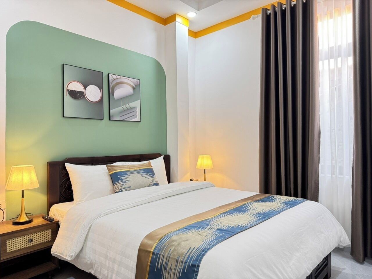A hotel room with a bed, two bedside lamps, a nightstand, and a wall with two framed pictures.