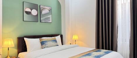 Une chambre d’hôtel avec un lit, deux lampes de chevet, une table de nuit et un mur orné de deux tableaux encadrés.