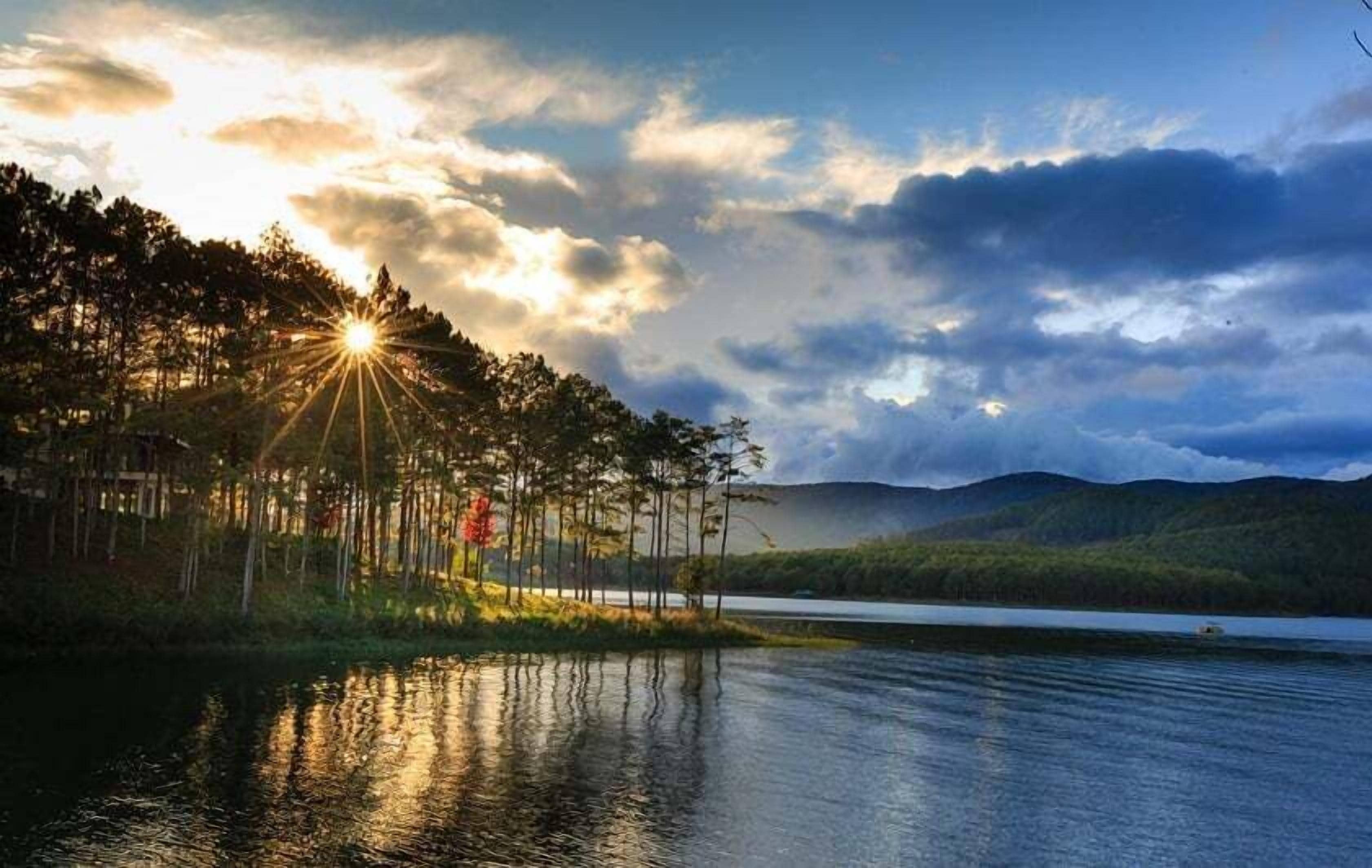 A serene lakeside view with a sunset, calm water, and a forested area.